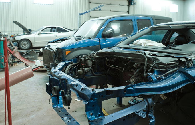 Car repair shop with damaged vehicles and repair equipment.