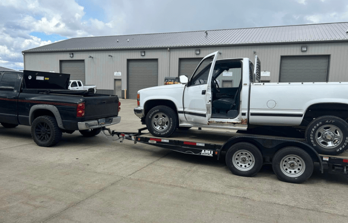 Tow truck transporting a white pickup truck at Above All Auto Repair facility.