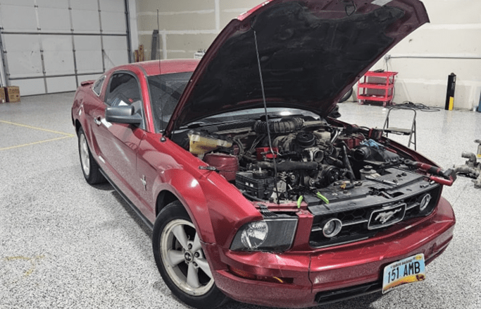 Red Ford Mustang with open hood in auto repair shop.
