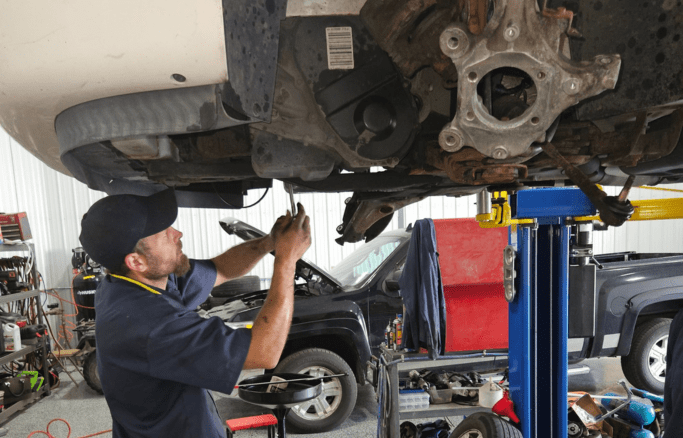 Auto repair technician inspecting underside of vehicle in a professional auto shop.