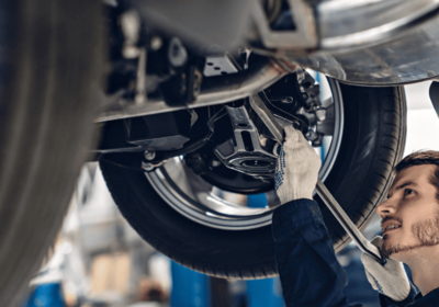 Auto repair technician inspecting vehicle underside at repair shop.