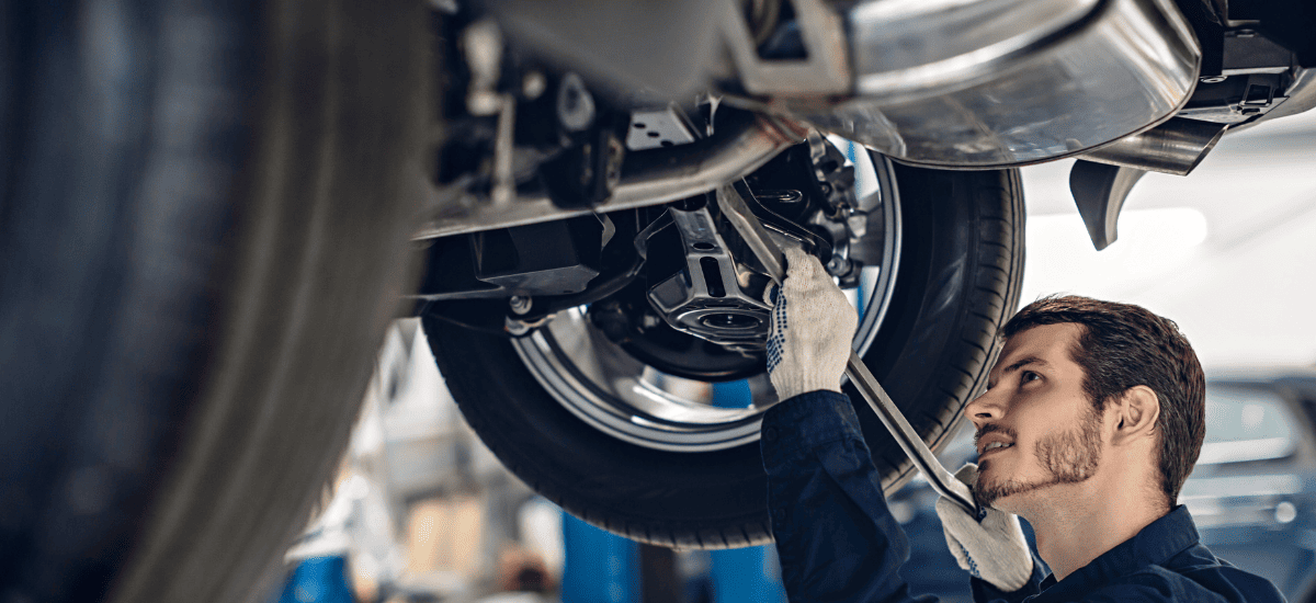 Auto repair technician inspecting vehicle underside at repair shop.