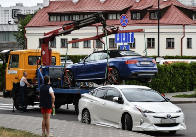 Towing a damaged blue car with a hydraulic lift on a flatbed tow truck in an urban setting.