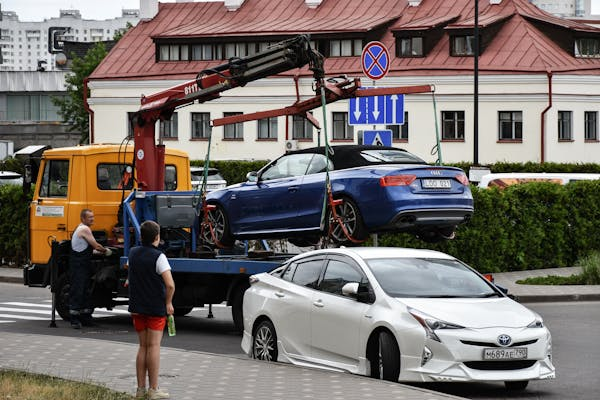 Towing a damaged blue car with a hydraulic lift on a flatbed tow truck in an urban setting.