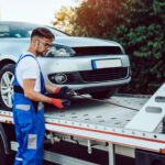 Auto repair technician inspecting vehicle on tow truck.