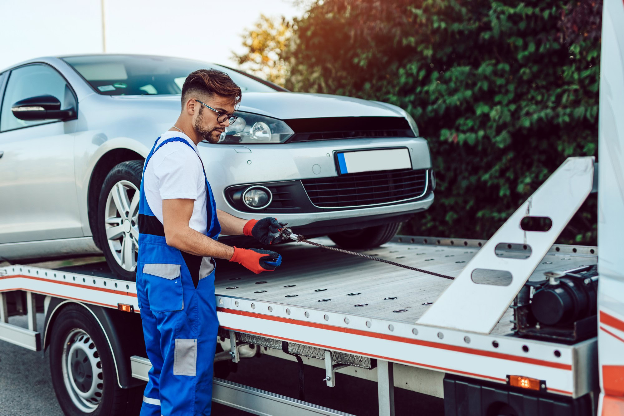 Auto repair technician inspecting vehicle on tow truck.