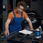 Engine repair technician inspecting car engine at auto repair shop.