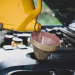 Mechanic pouring oil into car engine during oil change service at auto repair shop.