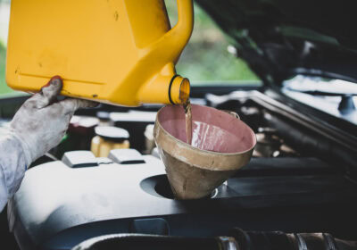 Mechanic pouring oil into car engine during oil change service at auto repair shop.