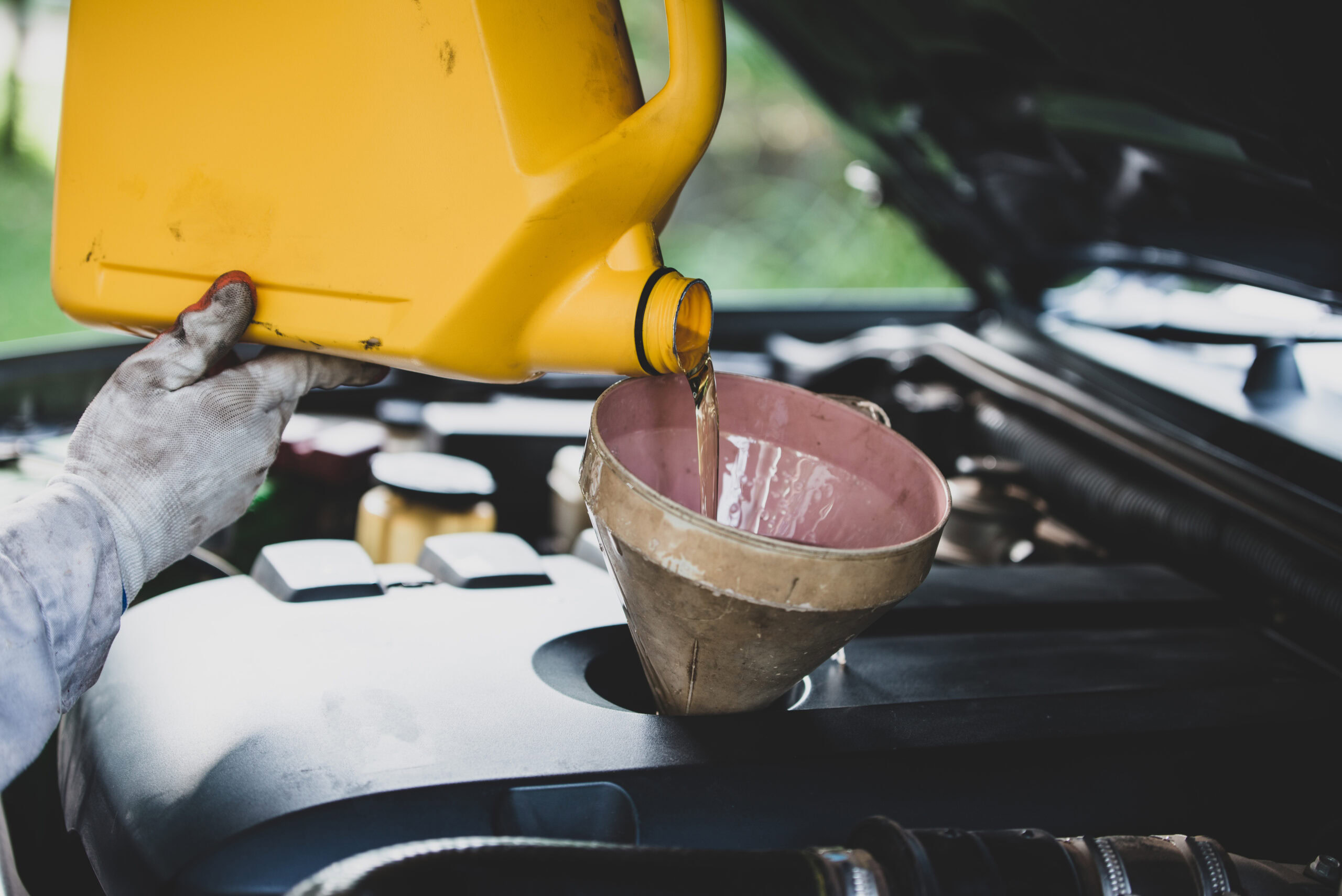 Mechanic pouring oil into car engine during oil change service at auto repair shop.