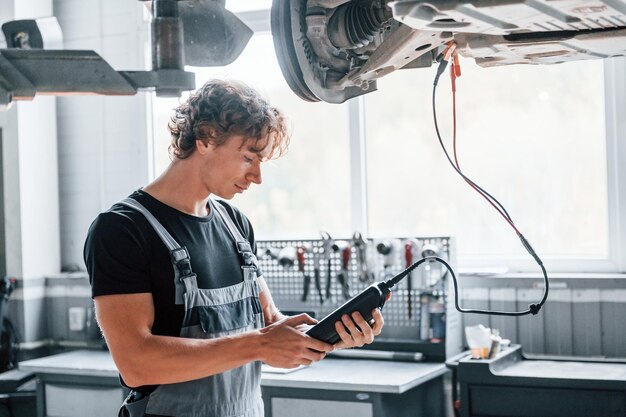 Auto repair technician inspecting vehicle undercarriage with diagnostic tablet.