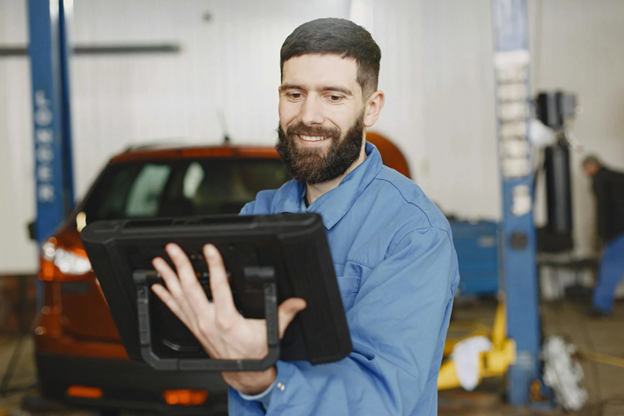 Technician using diagnostic scanner on vehicle in auto repair shop.