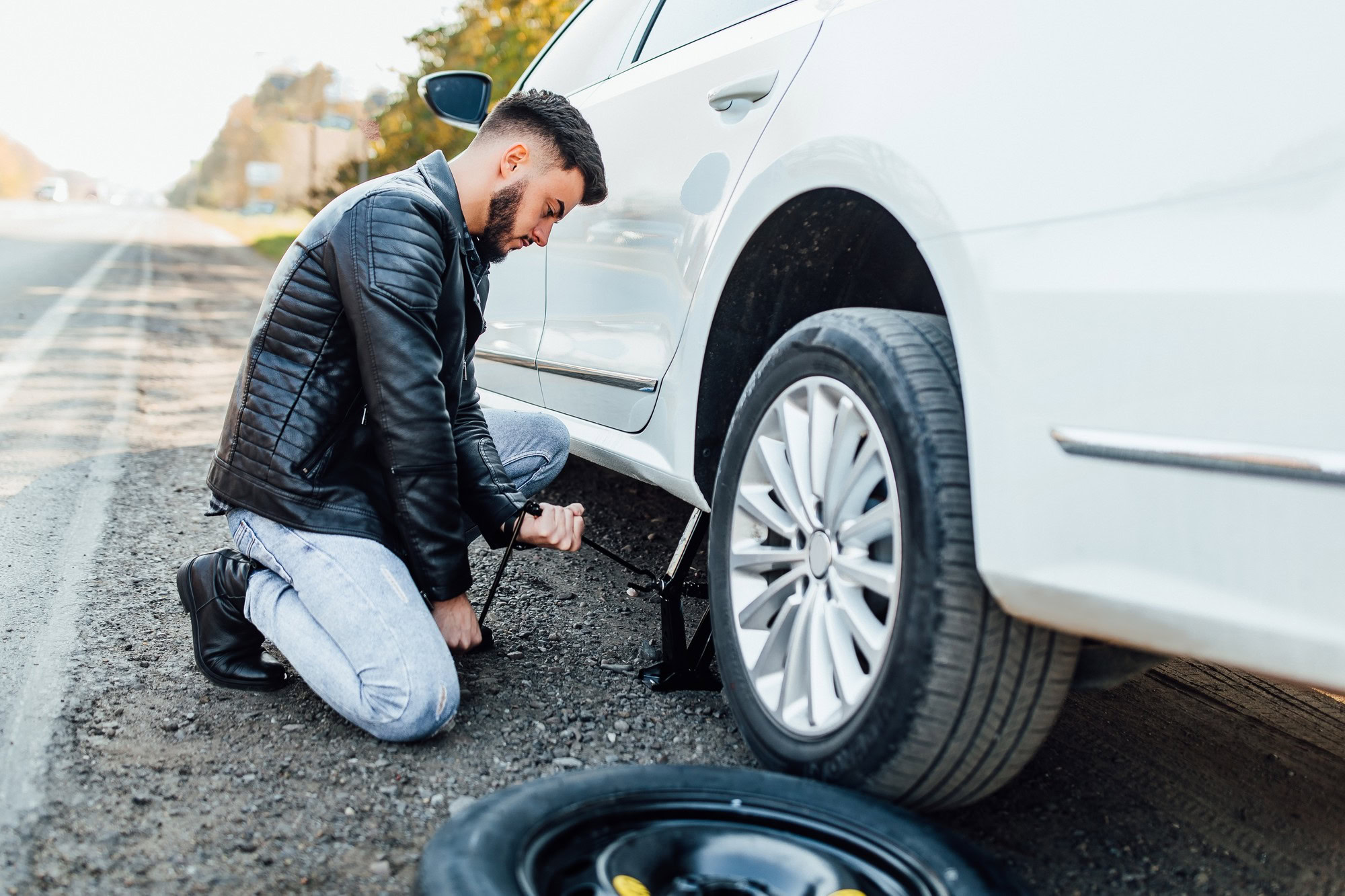 A man checking his car's tire on the roadside for wear and tear.