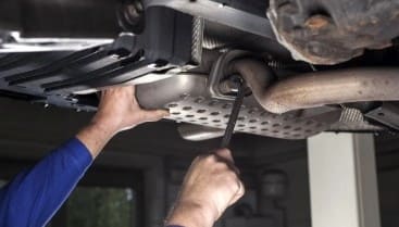 Technician performing oil change on a vehicle's underside at Al’s Automotive.