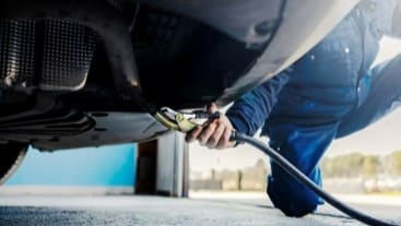 Technician performing oil change under a vehicle at Al’s Automotive.