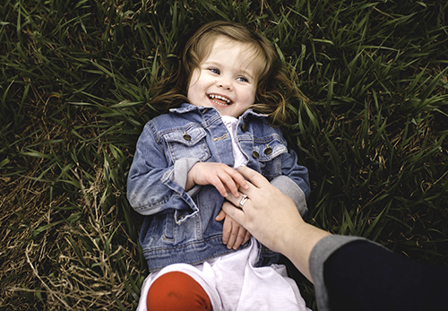 Young girl lying on grass, being tickled by her mother, overhead view
