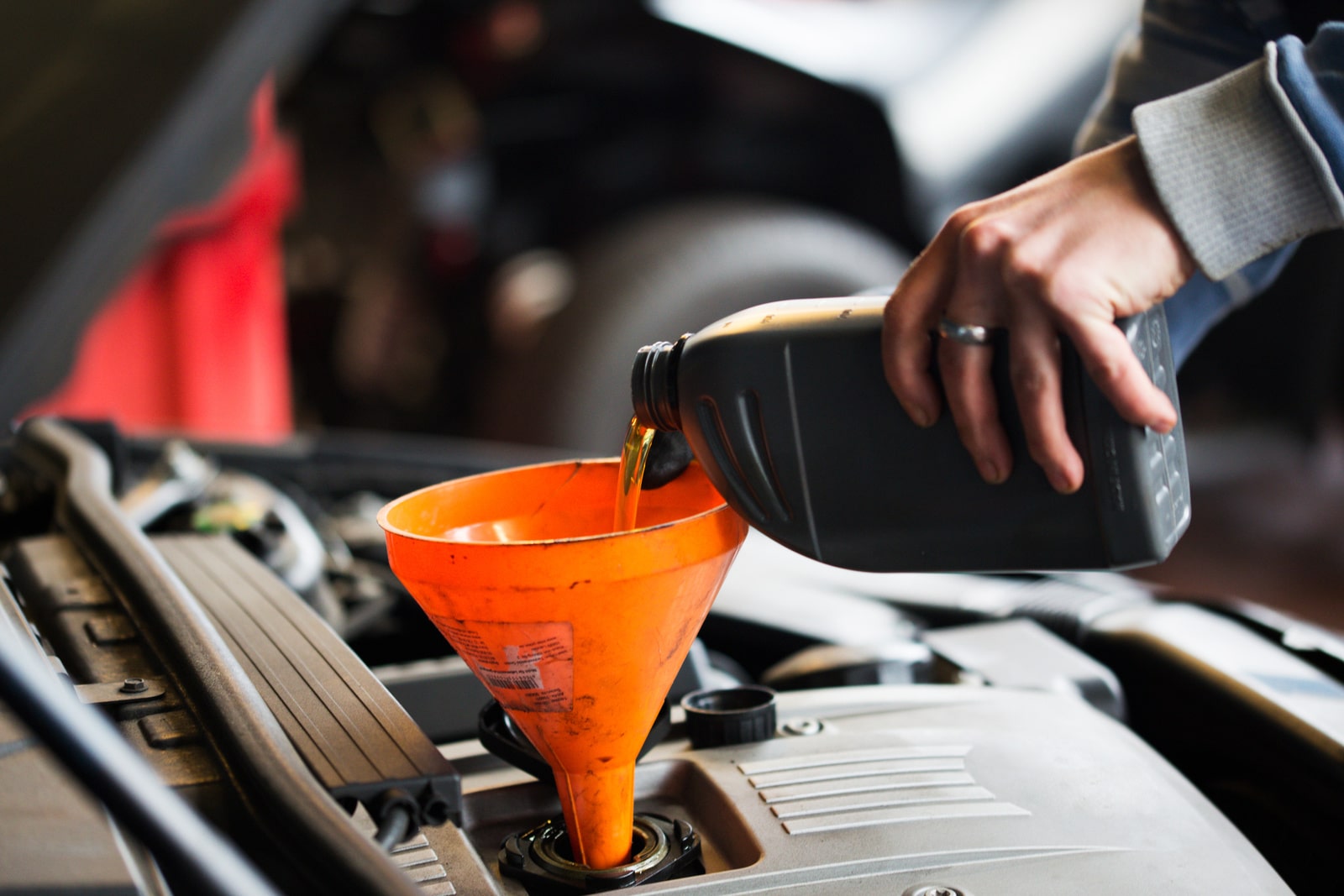 Mechanic pouring engine oil into car engine during maintenance.