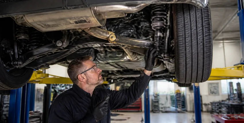 Automotive mechanic checking vehicle undercarriage in repair shop.