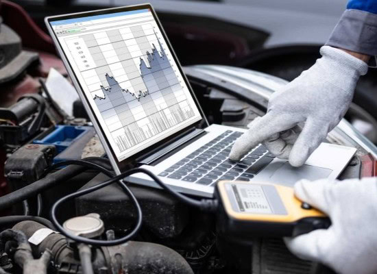 Auto repair technician using laptop for vehicle diagnostics at the repair site.