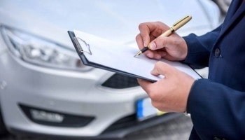 Technician inspecting a vehicle with a clipboard for maintenance check.