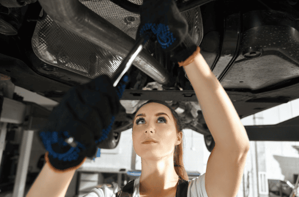 Woman inspecting car undercarriage for tire wear and damage.
