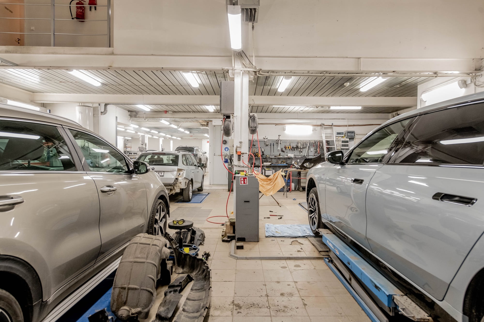 Car repair shop with two vehicles on lifts and tools in the background.