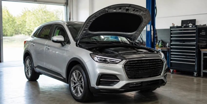 Silver SUV with open hood in auto repair shop for maintenance or repair.