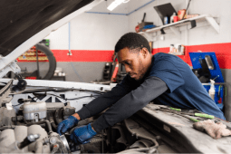 Technician repairing steering and suspension components in a vehicle engine bay.
