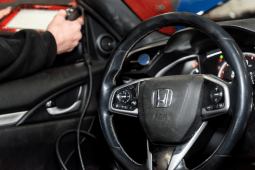 Technician inspecting steering wheel and suspension components in a car.