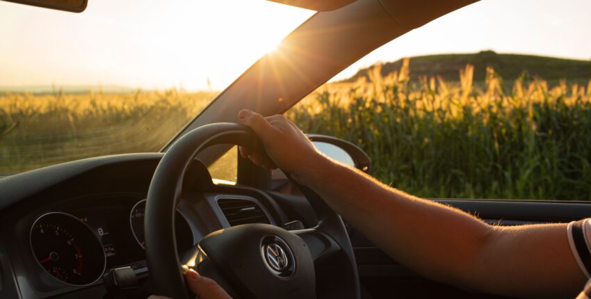 Person driving a car through open fields at sunset with scenic view.