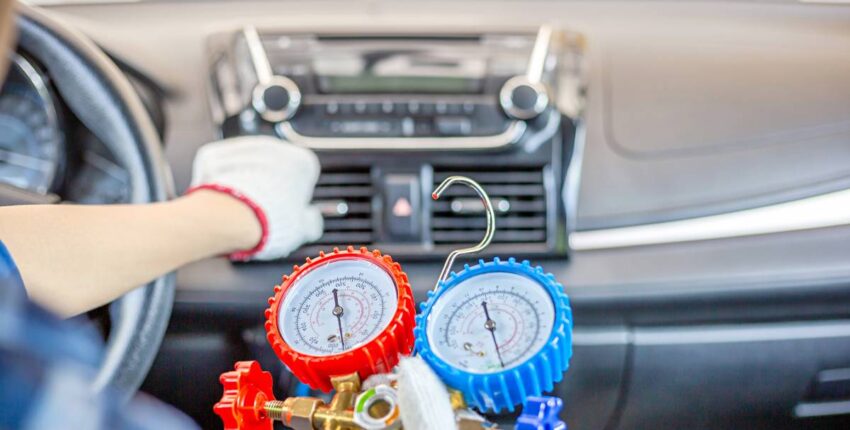 Technician checking car's air conditioning system with gauges inside vehicle.