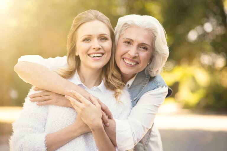 Sharing hugs. Smiling happy young woman walking in the park while expressing delight and hugging aging parent