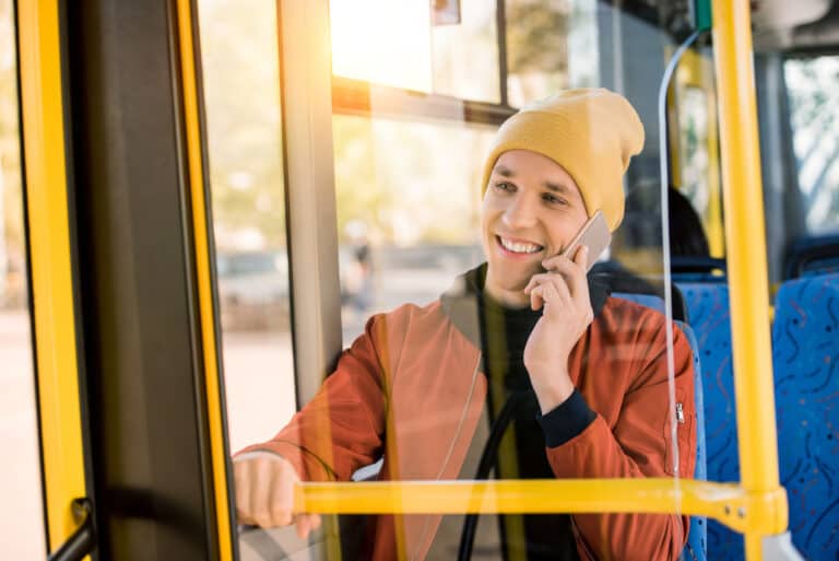 A young man sitting in a bus on the phone.