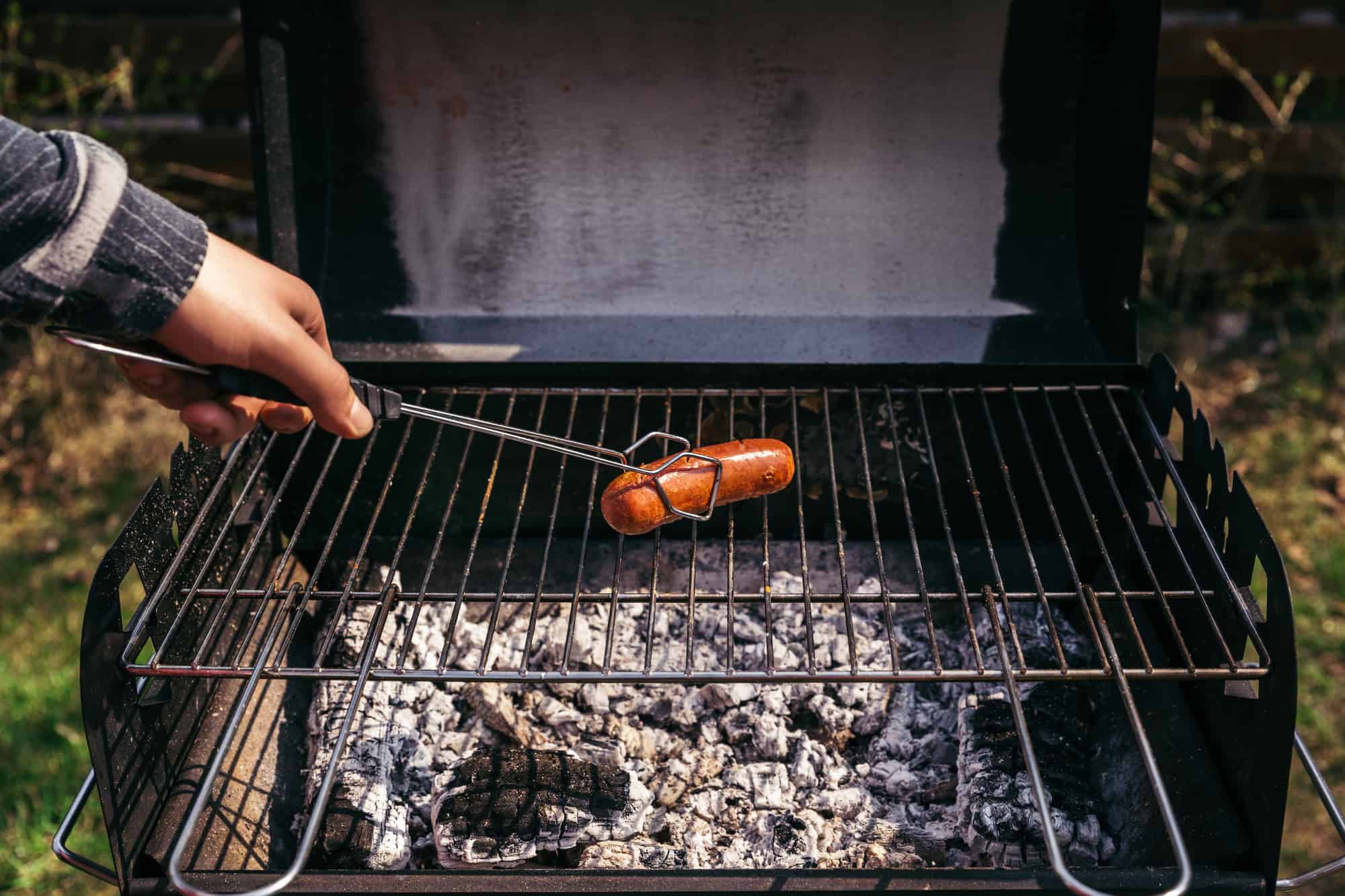 Man with serving tongs cooking sausages outdoors on grill. Food. BBQ.
