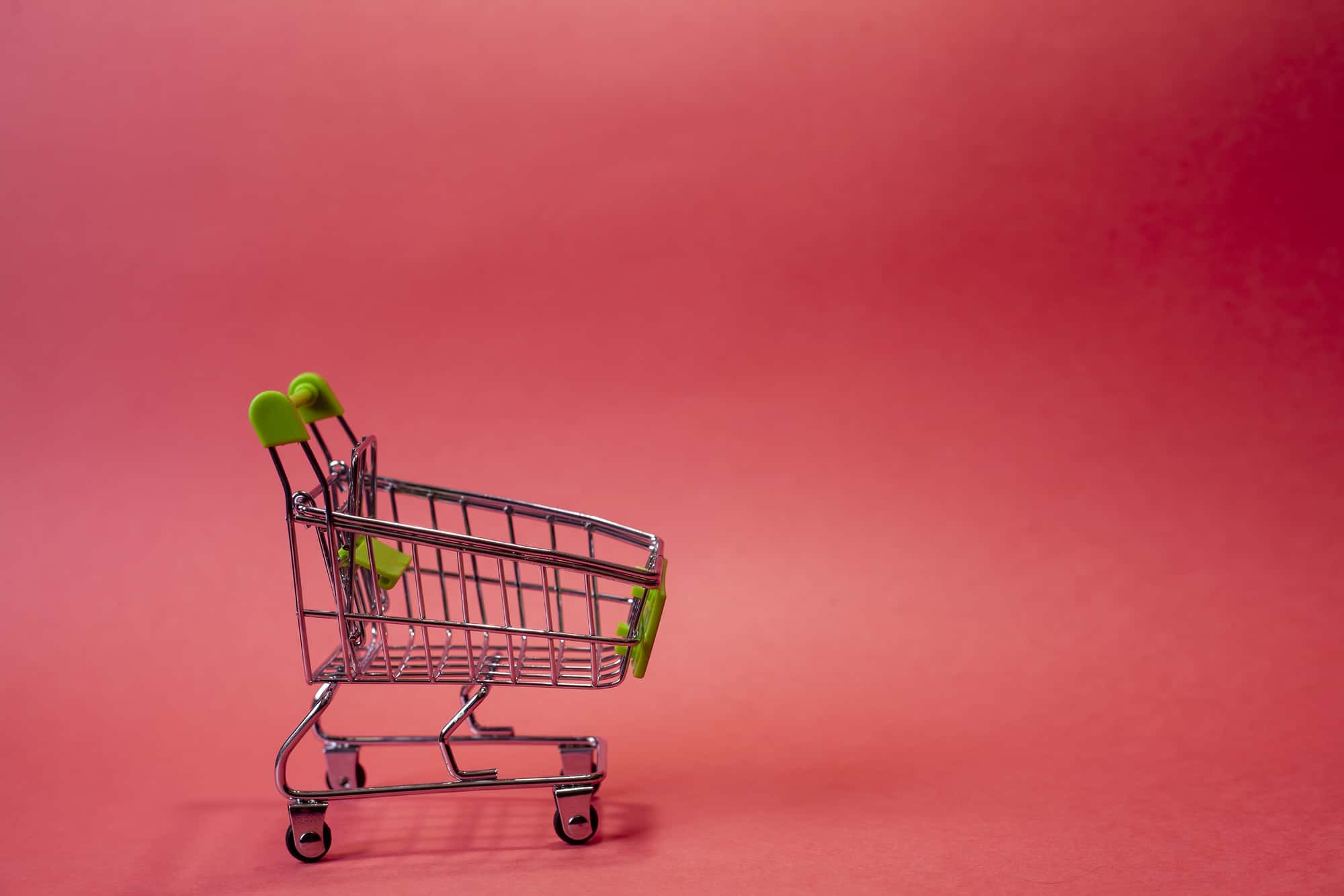 Tiny shopping cart on the red background with space for text