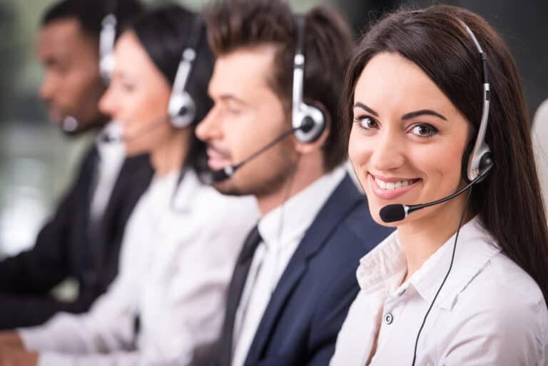 Side view of line of call centre employees are smiling and working on computers and with headset on.