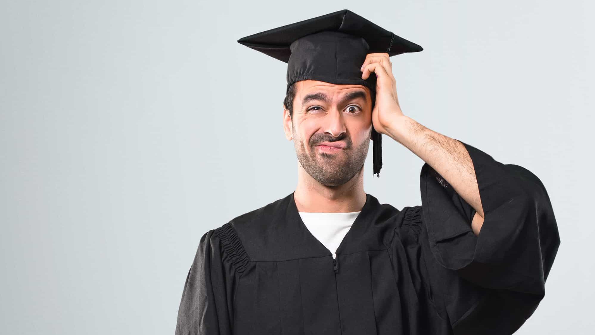 Man on his graduation day University with an expression of frustration and not understanding. Confused gesturing on grey background. College graduate.
