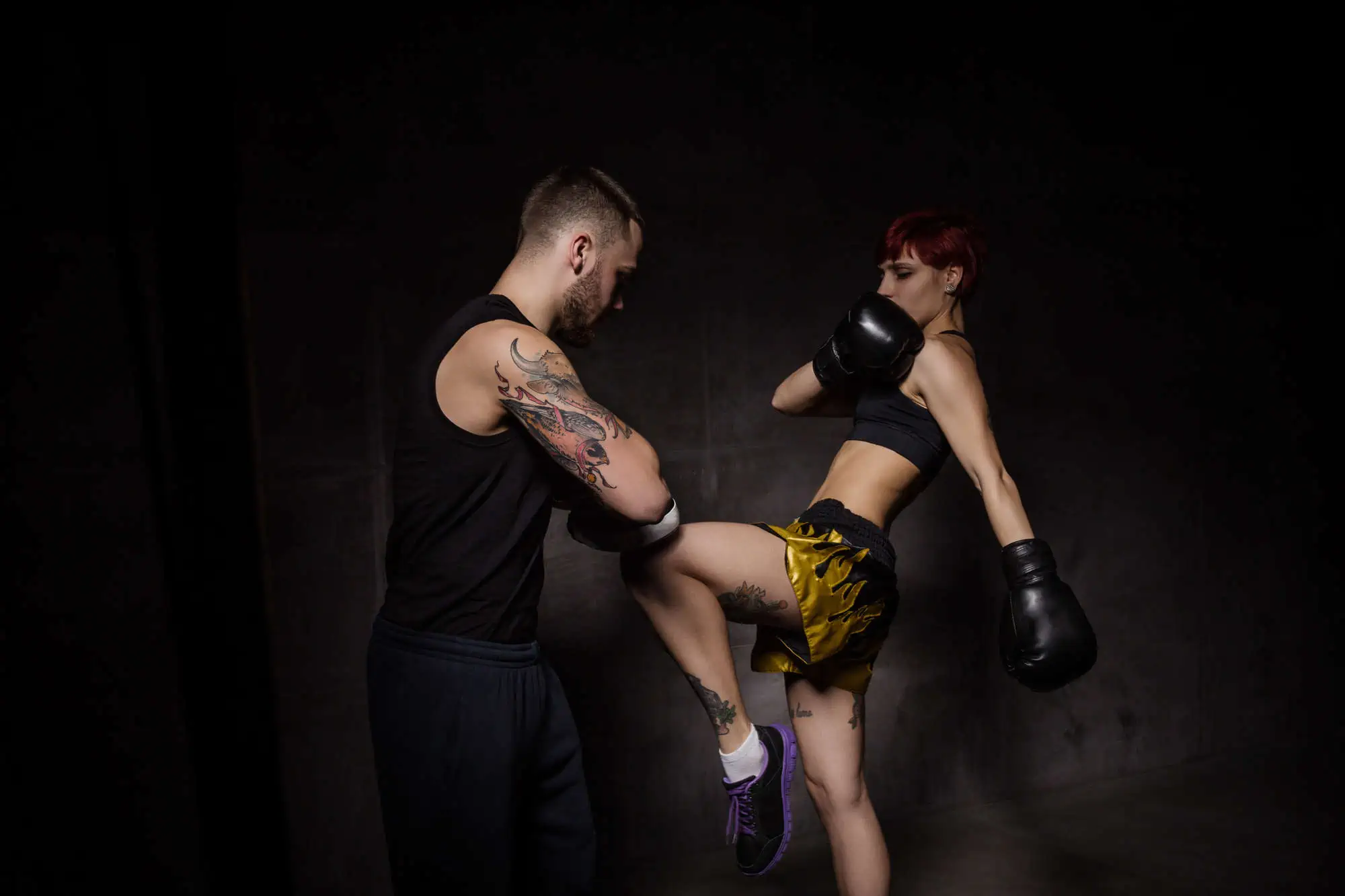 Woman boxer hitting training mitts held a boxing trainer in dark room