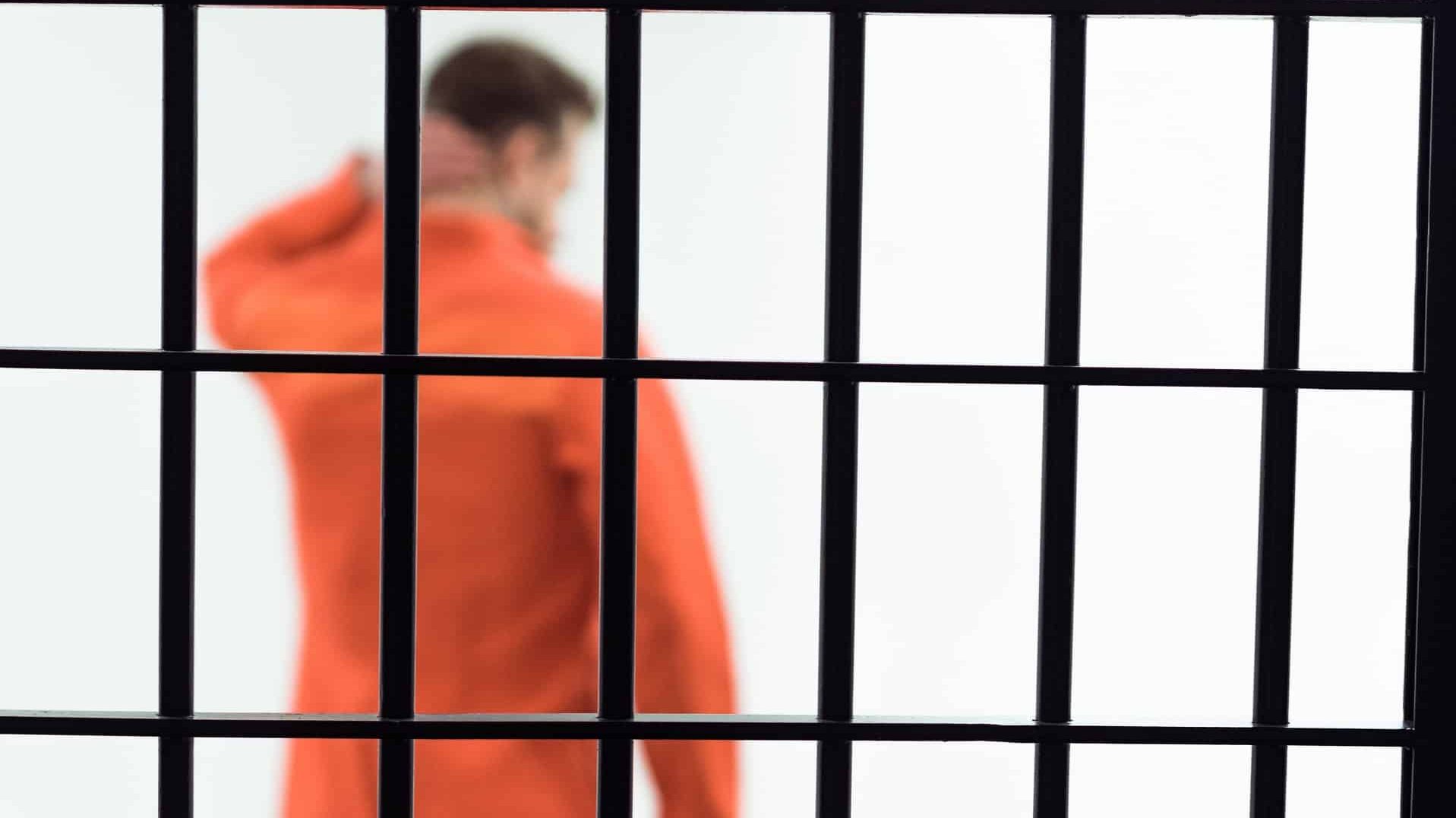 Rear view of prisoner in prison cell with metallic bars on foreground