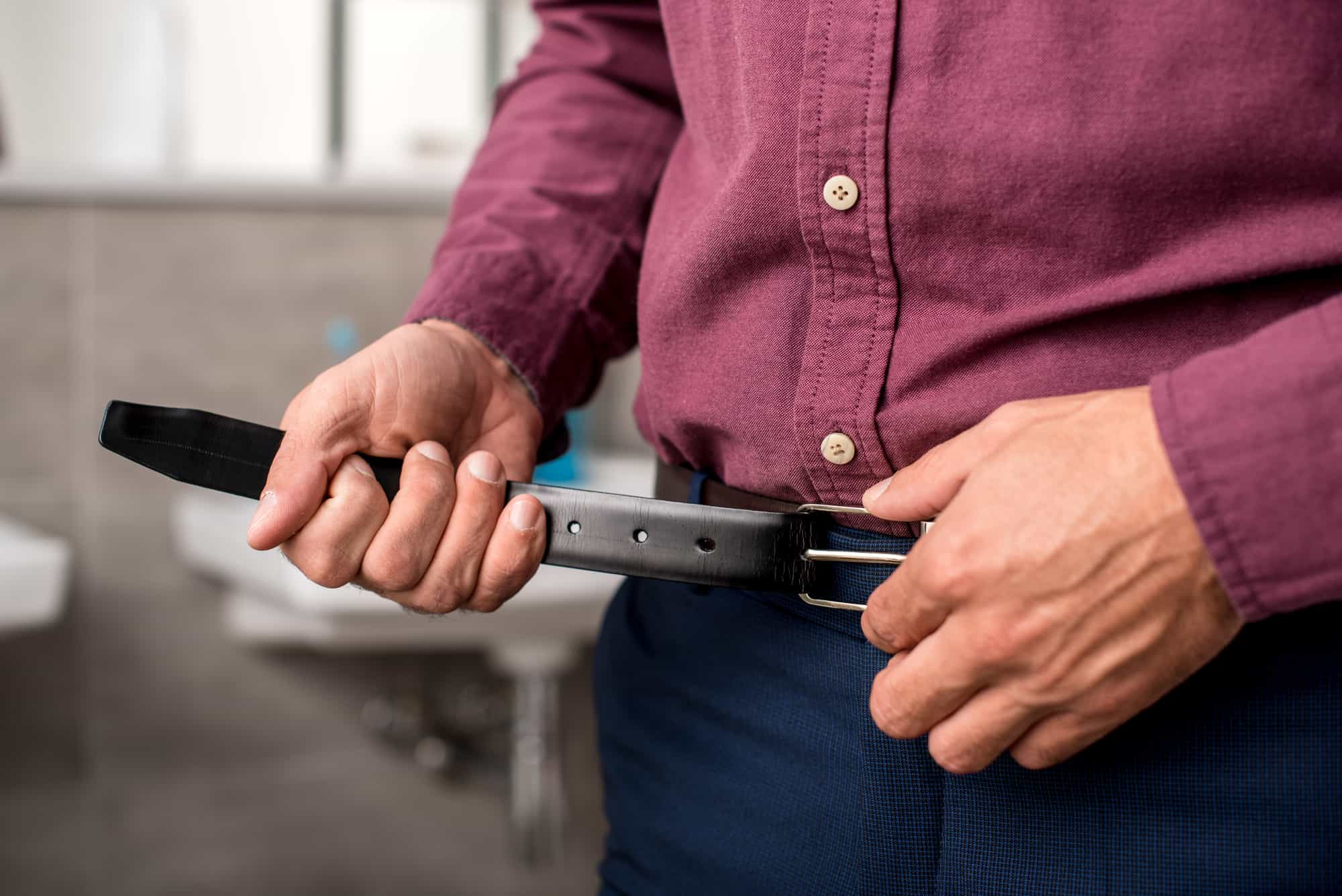 businessman putting on belt at home