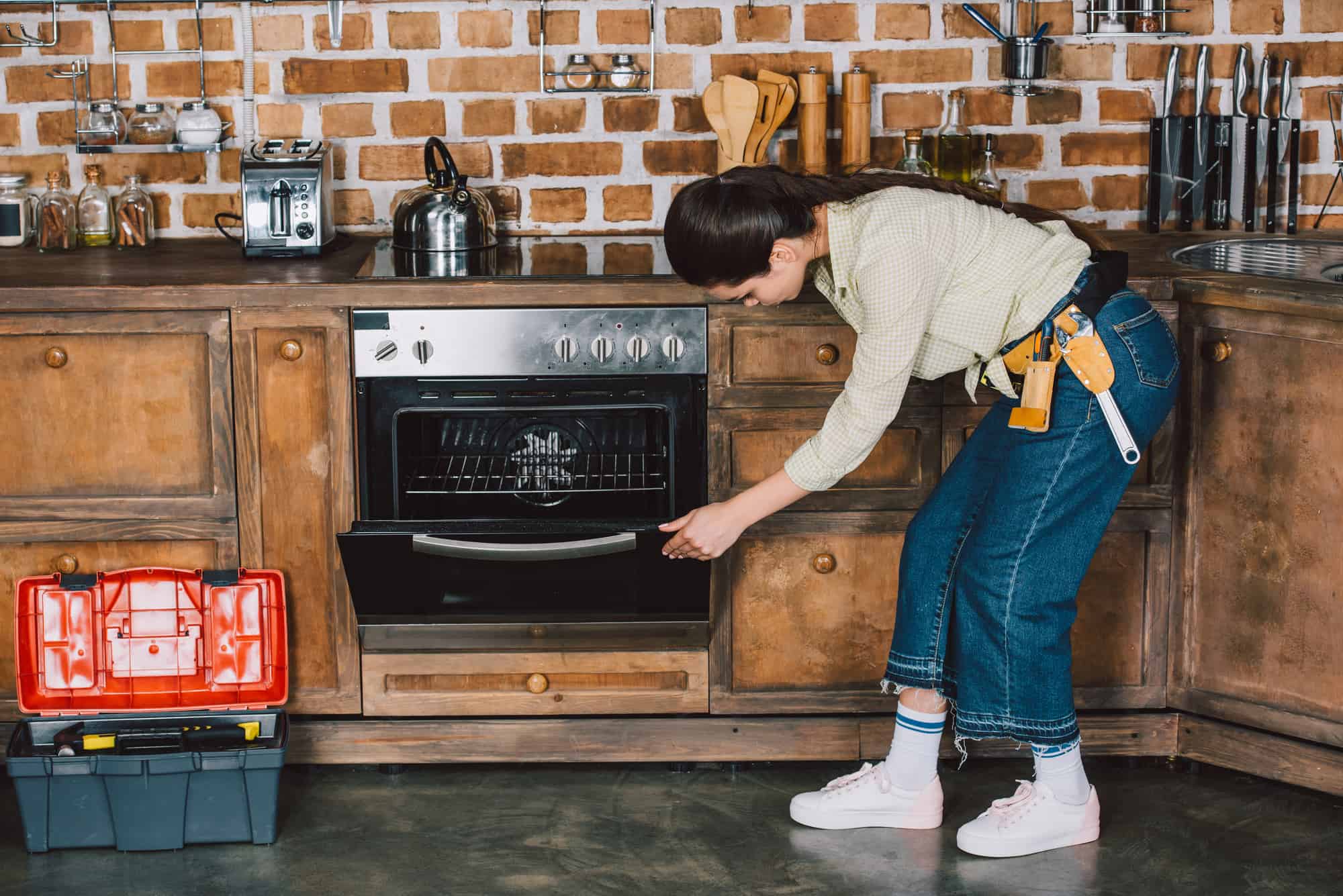 Confident young repairwoman examining oven at kitchen