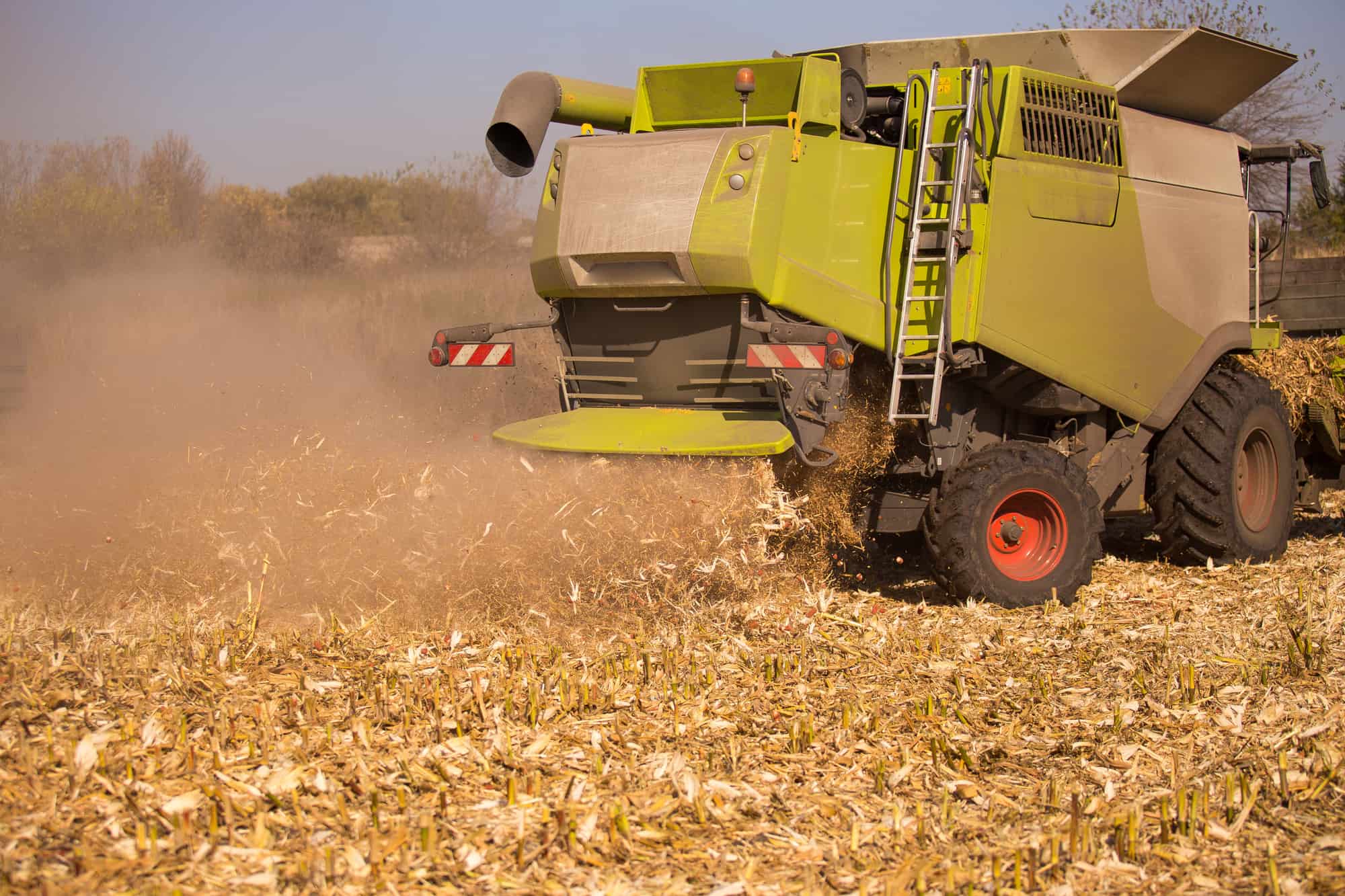 The theme is agriculture. A modern combine harvester in the field performs grain harvesting on a sunny day against a blue sky. Farm and automation using machines