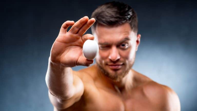 Muscled male holds a fresh chicken organic egg in his hand and points to the camera. Healthy lifestyle concept.