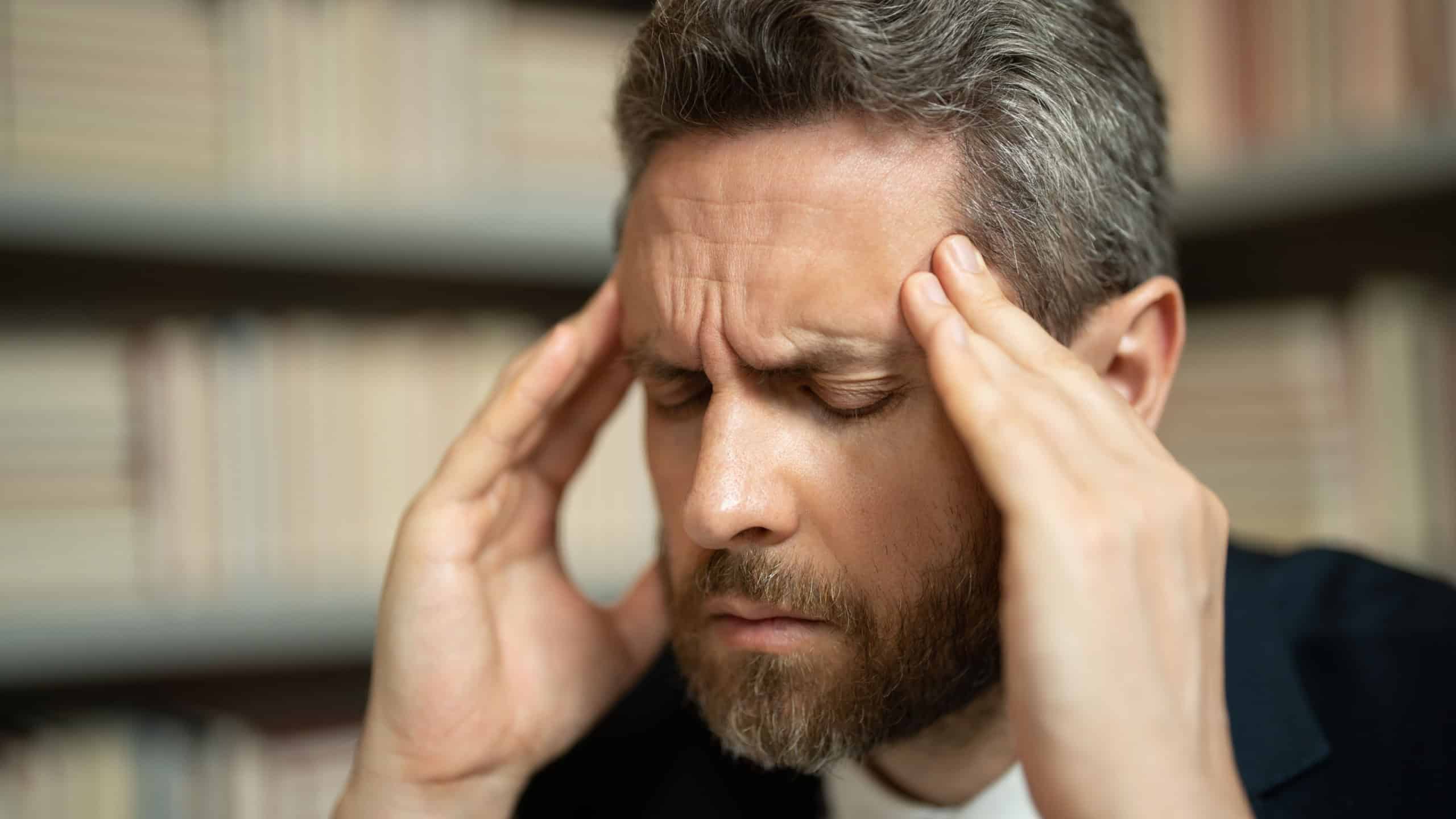 Close up portrait of stressed man with headache migraine. Stressed man with headache. Tired businessman is working overtime and has headache. Man with laptop at workplace, suffers from headache.