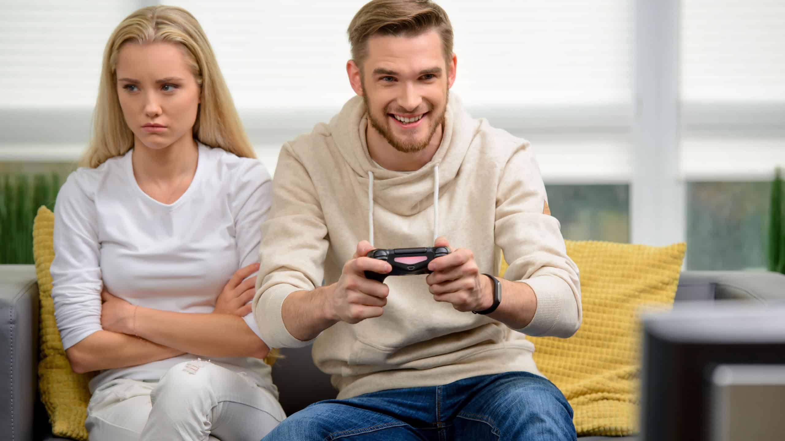 Video games concept. Young annoyed girlfriend waiting for her boyfriend to stop playing video games. Nice apartment interior