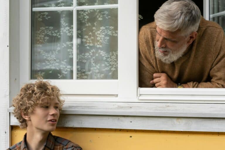Teenager Standing Near Wall and Grandfather Leaning out of Window