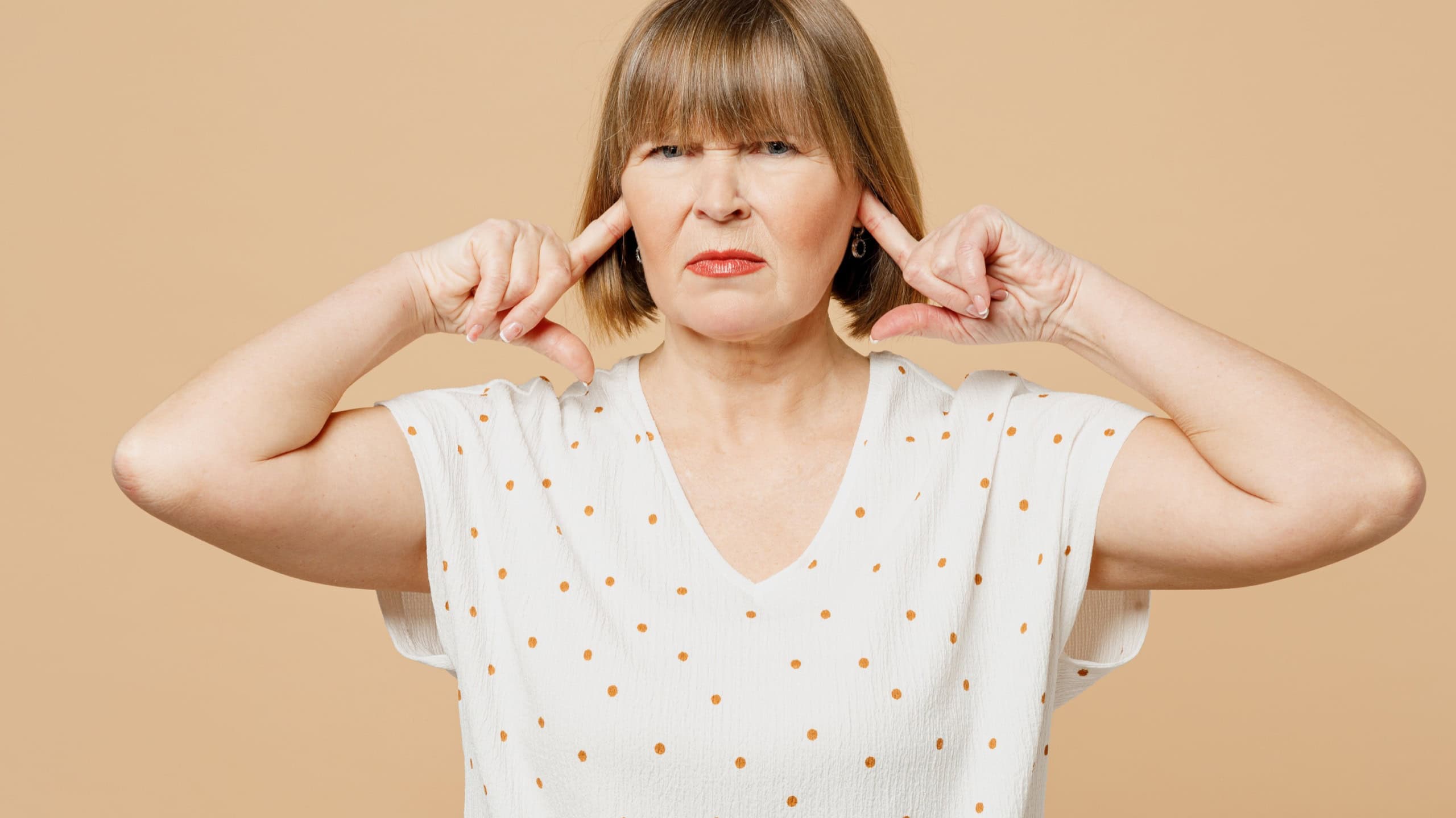 Sad blonde annoyed indignant elderly woman 50s years old she wear casual clothes cover ears with hands fingers do not want to listen scream isolated on plain light beige background. Lifestyle concept