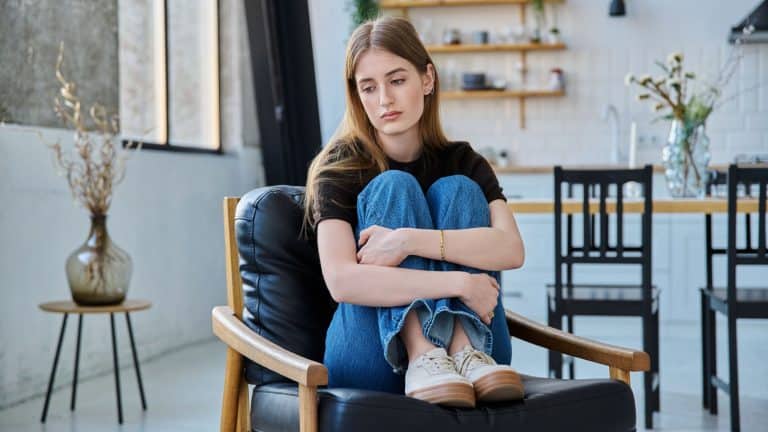 Sad stressed young woman sitting at home on armchair