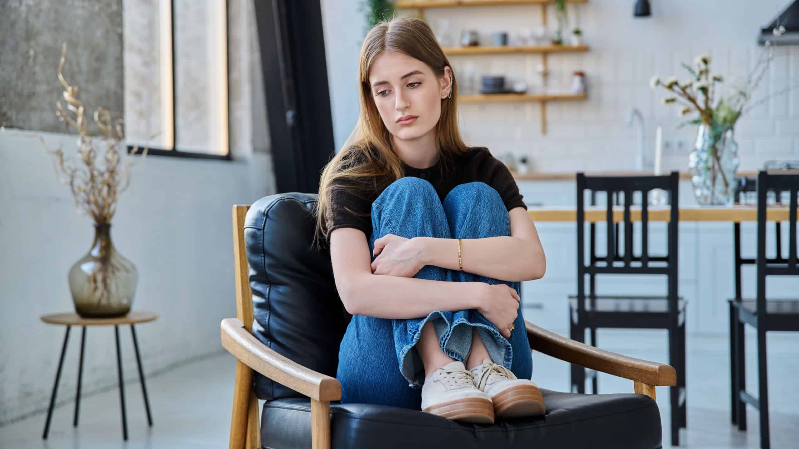 Sad stressed young woman sitting at home on armchair
