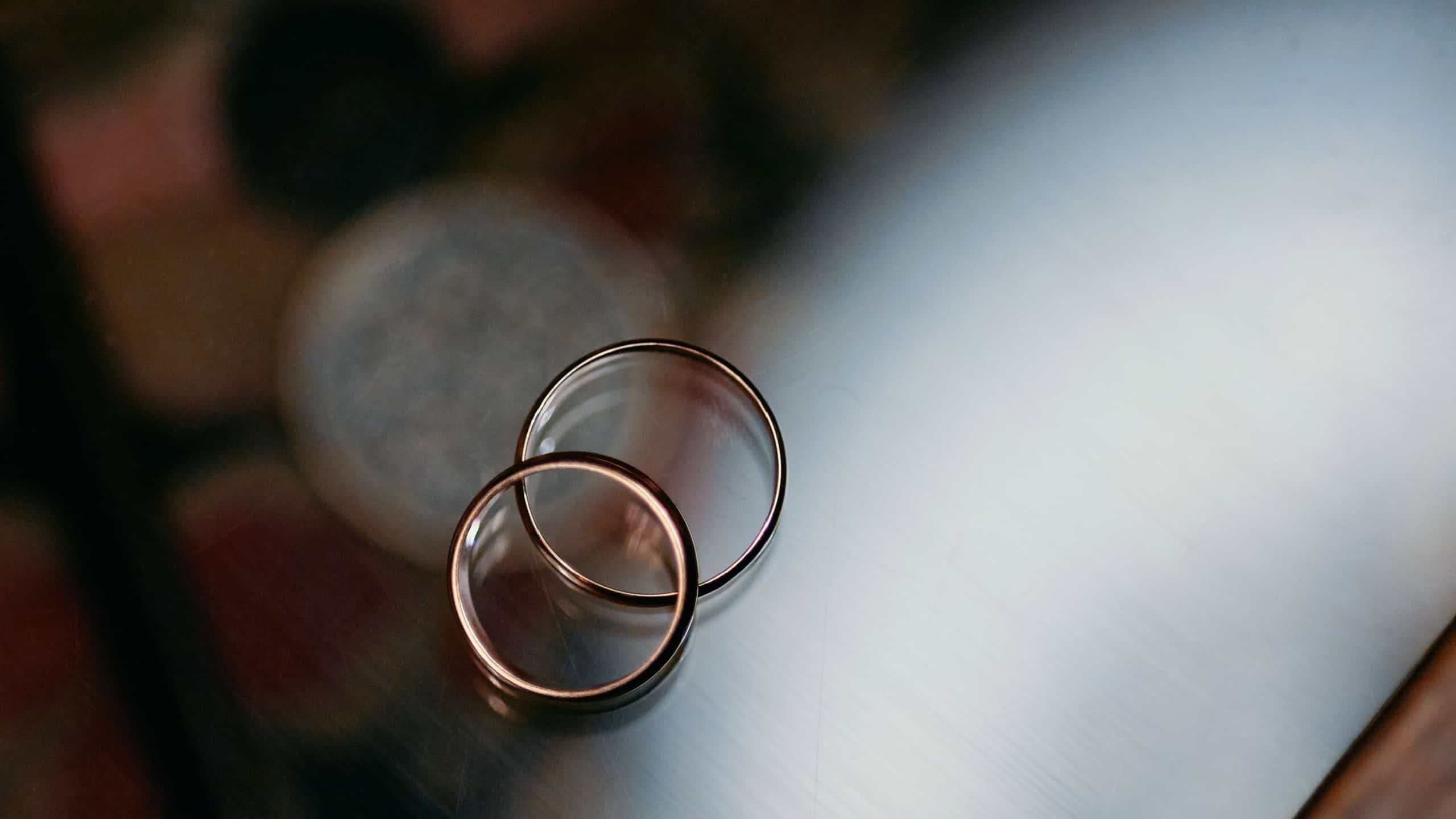Two gold wedding rings placed together on a glass surface symbolize love, unity, and commitment. The minimalist setup highlights the symbolic nature of marriage and togetherness.